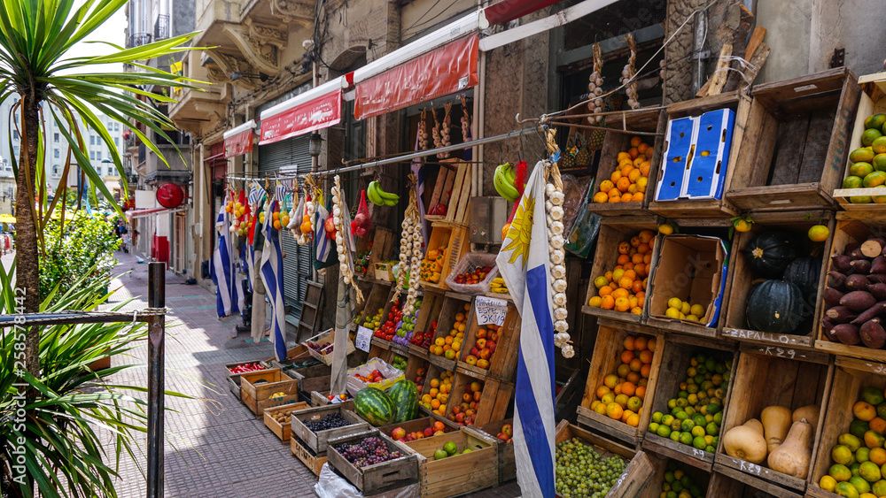 A street with a fruit stand with boxes piled with fruits.