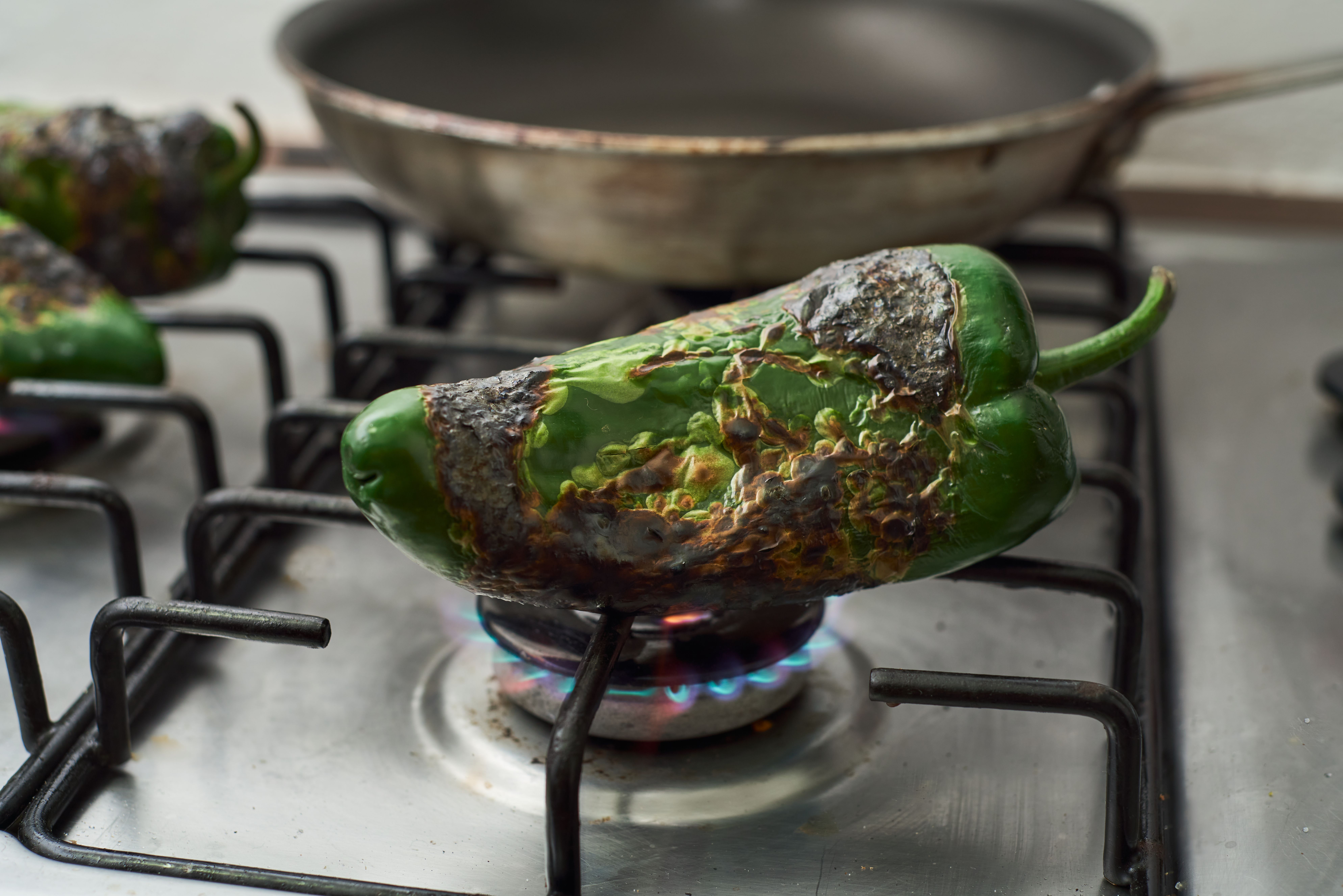 A charred poblano pepper on top of a natural gas burner on a stove.