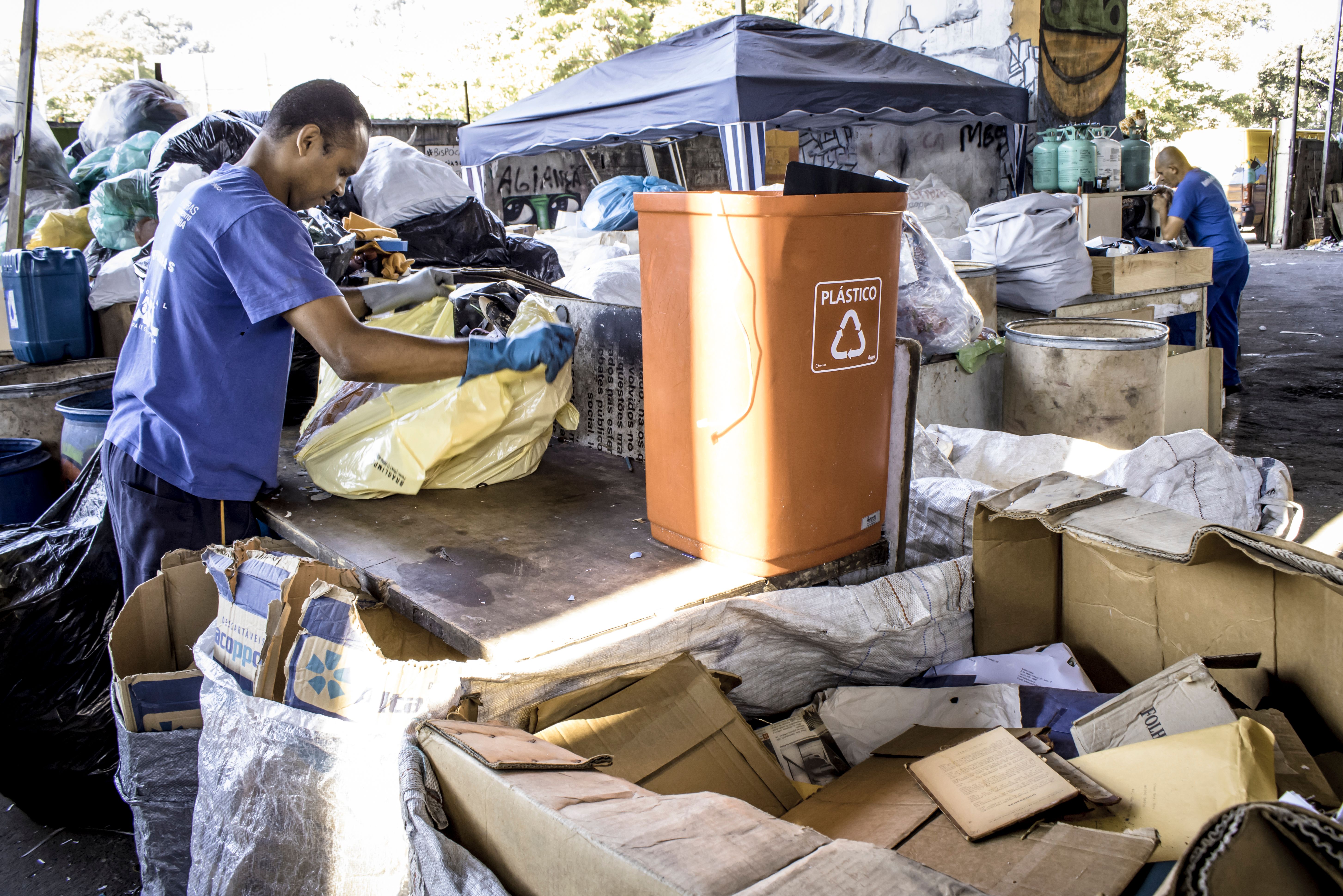 Workers from a waste picker cooperative stand at tables sorting waste.