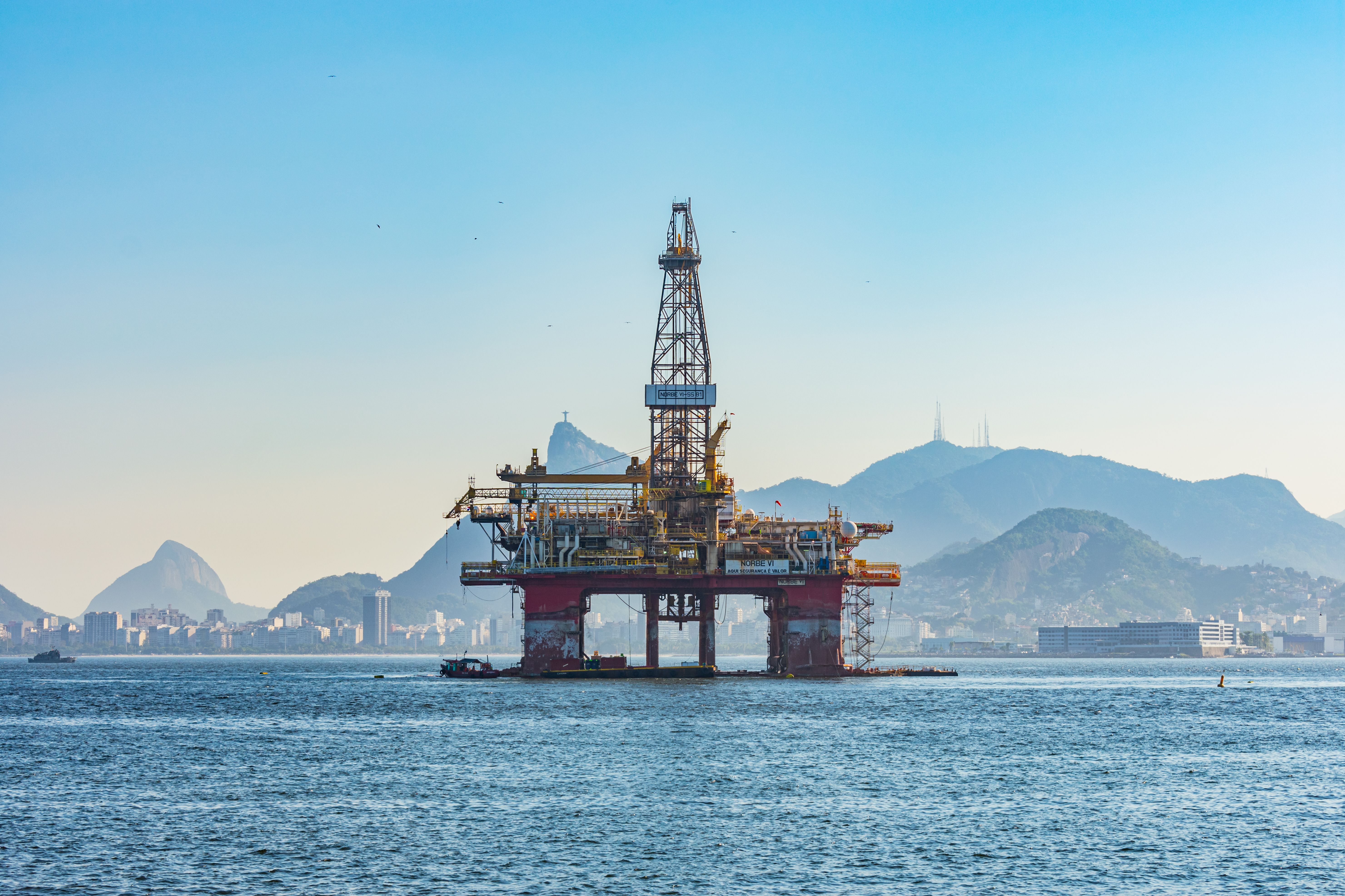 An oil exploration platform in the middle of a water body with Rio de Janeiro in the background.